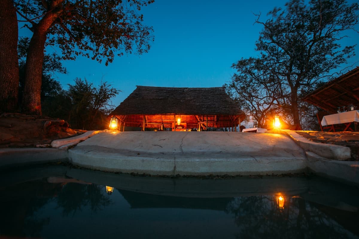 A thatched-roof safari lodge lit at dusk beside a plunge pool
